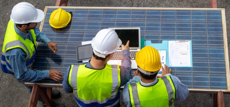 Top view of technical professionals team in safety helmets and uniforms contemplating a new project with solar photovoltaic panels
